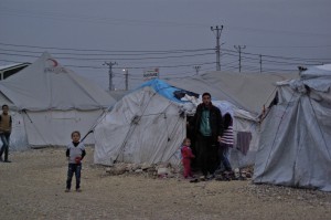 Eine junger syrischer Vater steht mit seinen Kindern vor einem Zelt.